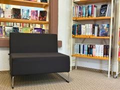 Ein Sessel steht in der Mediathek, dahinter verschiedene Bücher.