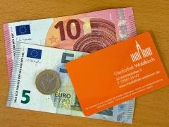 Auf einem Holztisch liegen 16 Euro und ein Mediatheksausweis.