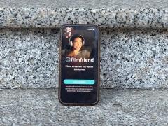 Auf grauen Stufen steht ein Handy. Auf dem Handy ist Filmfriend geöffnet.