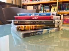 Auf einem Glastisch in der Mediathek liegt ein Stapel DVDs.