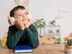 Ein Kind sitzt an einem Küchentisch und hört ein Hörbuch. Es hat Kopfhörer auf.