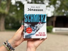 Das Buch Schmerz wird von einer Person in einem Park hochgehalten.