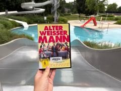 Eine DVD wird in einem Schwimmbad vor einer Rutsche hochgehalten.