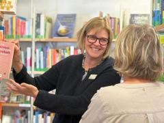 Eine Mitarbeiterin der Mediathek zieht ein Buch aus einem Regal. Vor ihr steht eine Kundin.