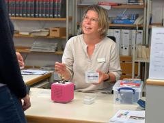 Eine Mitarbeiterin erklärt an der Theke der Mediathek einer Kundin die Toniebox. Die Toniebox steht auf der Theke.