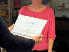 Eine Kundin nimmt einen weißen Umschlag der Fernleihe von einer Mitarbeiterin der Mediathek entgegen.