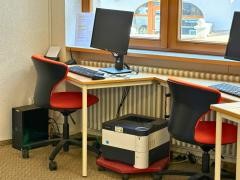 Auf einem Tisch steht ein Computer. Davor steht ein Schreibtischstuhl.
