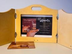 Auf einem Tisch steht eine Bühne aus Holz. In der Bühne ist ein Bild eingeklemmt.