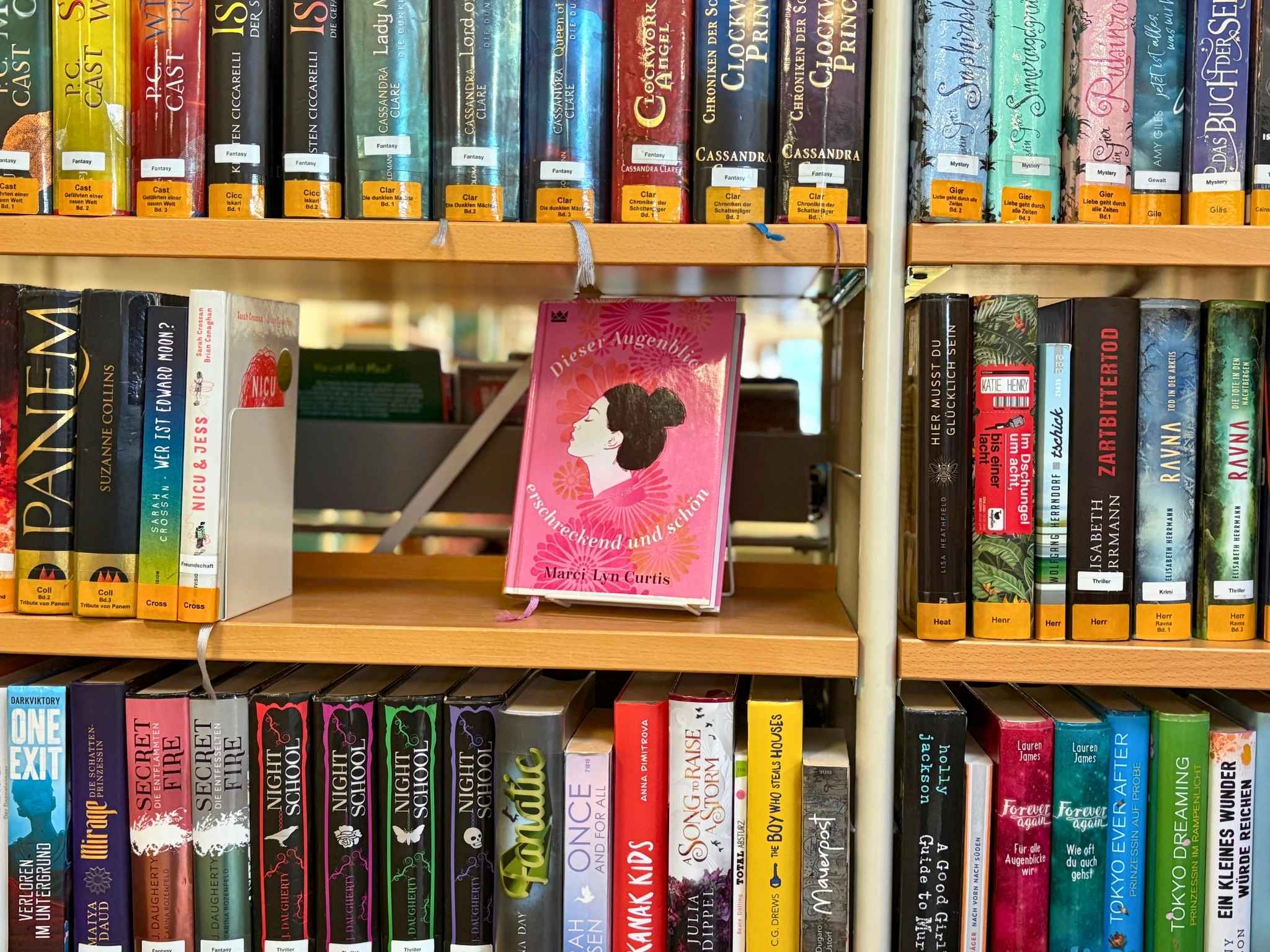 Foto eines B&uuml;cherregals. Im Fokus ist ein Buch mit rosa Cover.