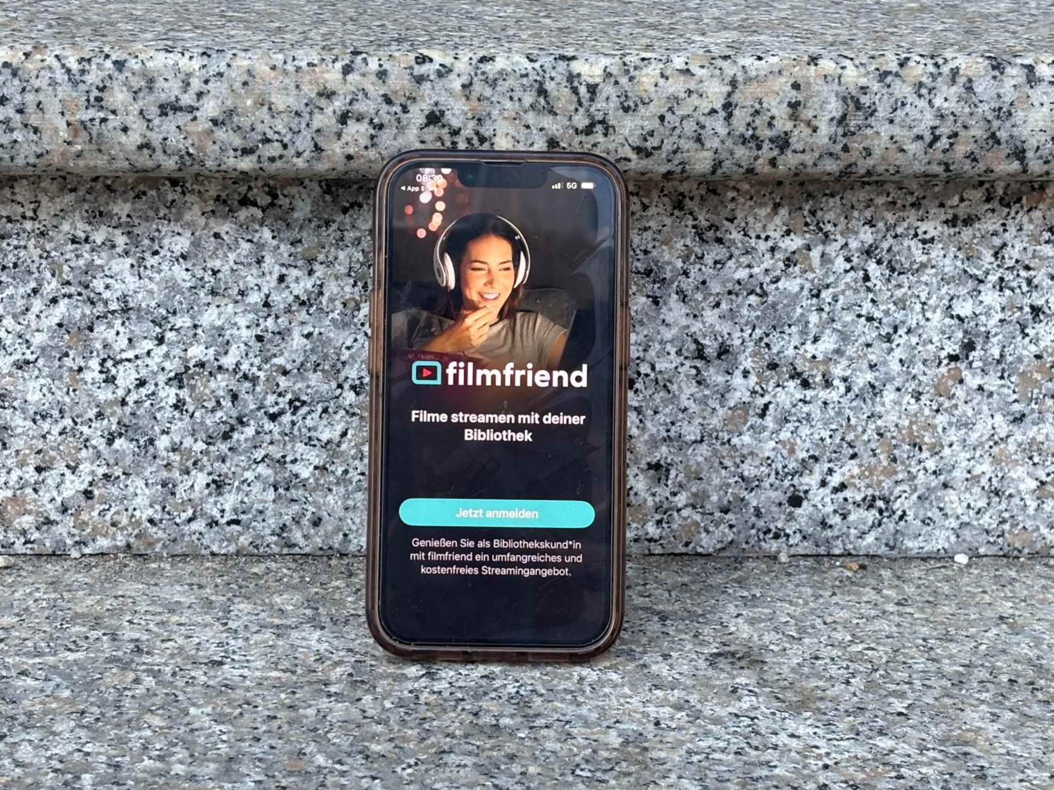Auf grauen Stufen steht ein Handy. Auf dem Handy ist Filmfriend ge&ouml;ffnet.