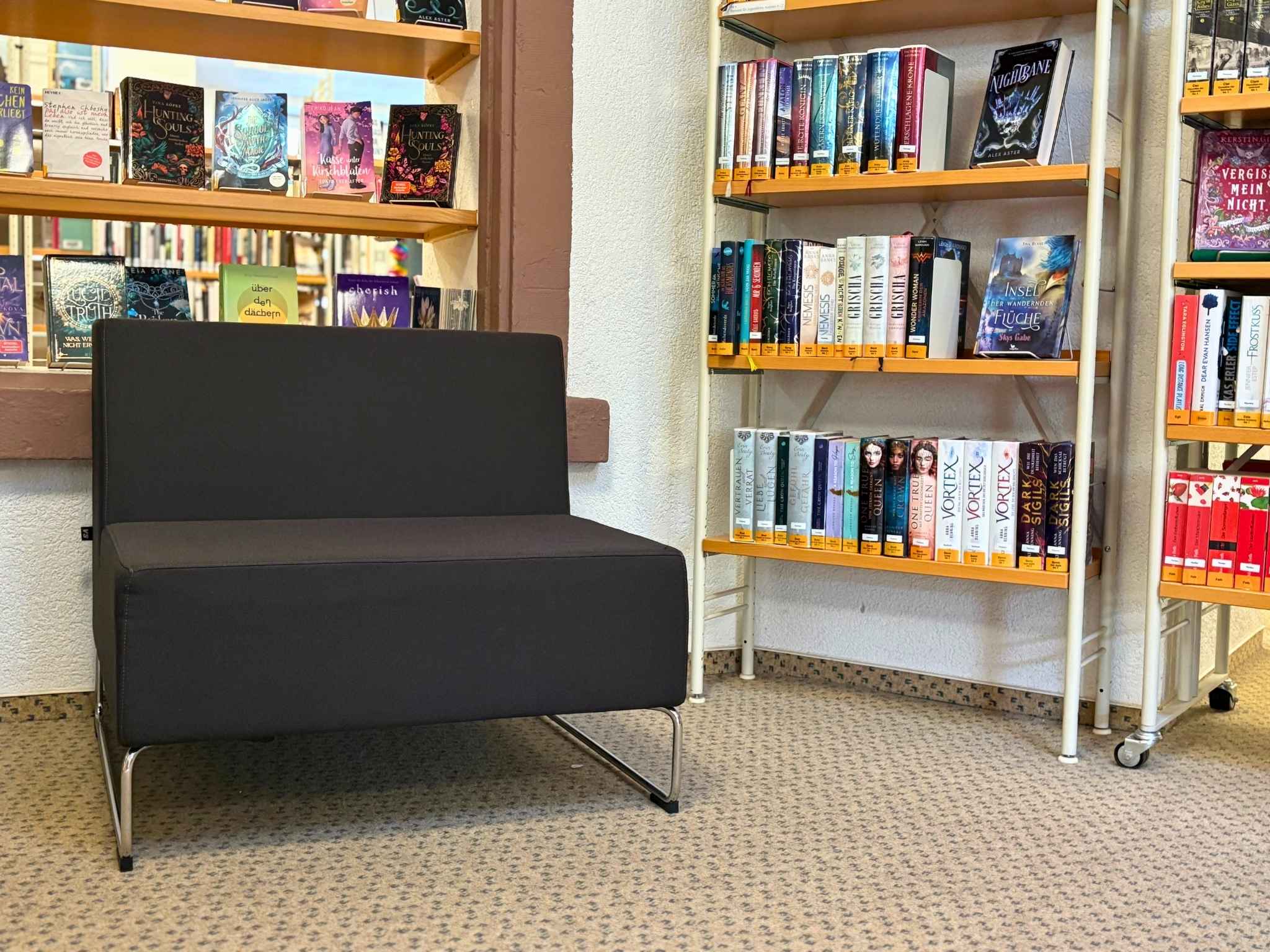 Neben einem B&uuml;cherregal in der Mediathek steht ein schwarzer Sessel.